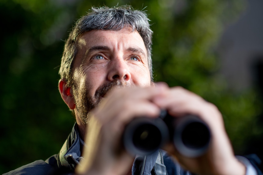 A man holding binoculars with looking contently up at the sky. 