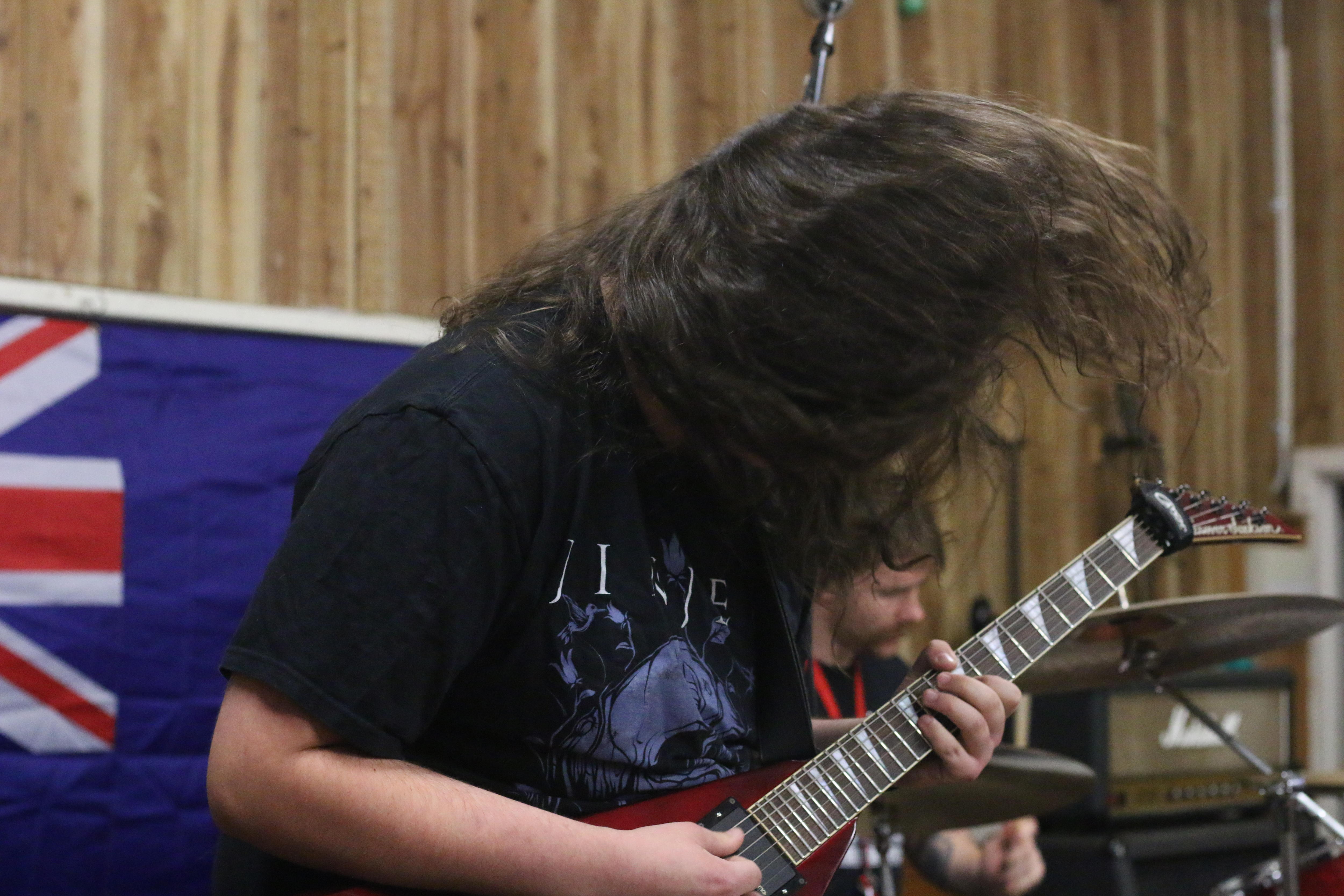 Um homem toca violão. Seus longos cabelos obscurecem seu rosto.