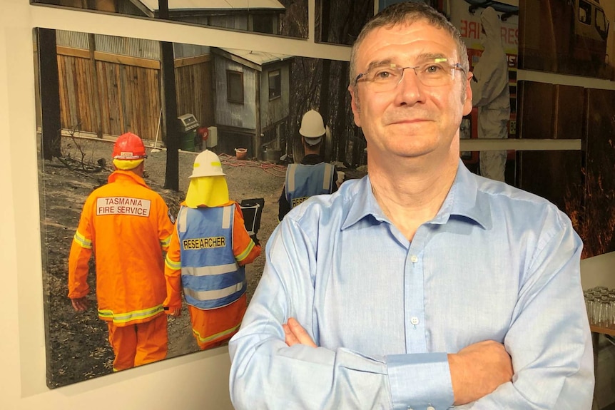 Richard Thornton, dressed in office attire, stands in front of an image of firefighters on a fire ground.