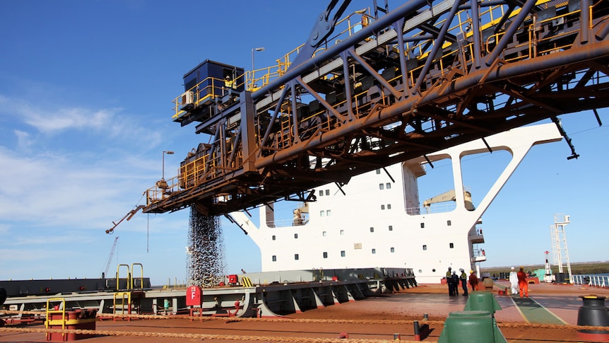 A horizontal crane pumps ore into the hold of a loading ship with superstructure visible in the Pilbara in 2012.