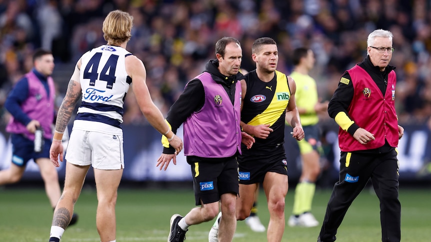 A Geelong player moves close watching as a Richmond player is helped off the field.