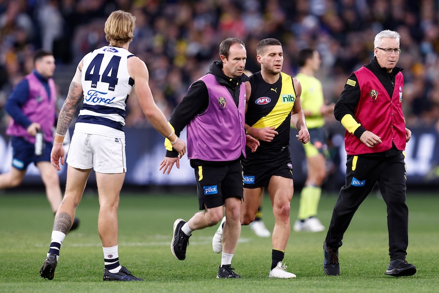 A Geelong player moves close watching as a Richmond player is helped off the field.