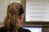 A woman with her hair in a ponytail looks at a laptop