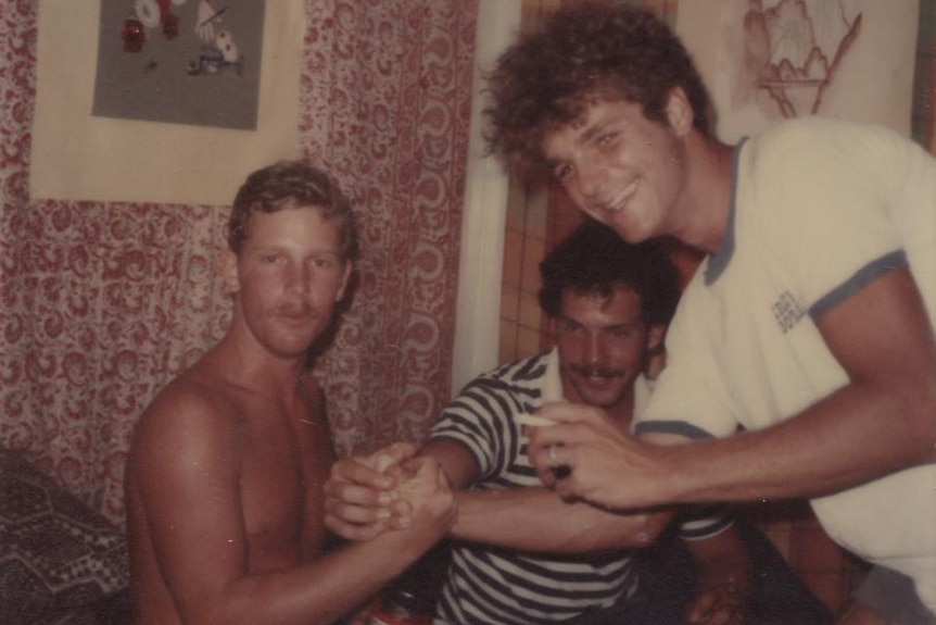 Three men pose in a three-way handshake at a party on Enewetak.