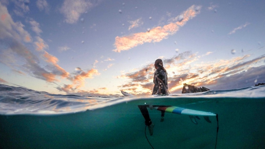 A surfer watches the sunrise from his board.