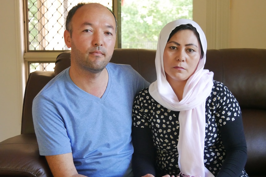 A man in a blue shirt and a woman in a pink head scarf sit on a couch together.