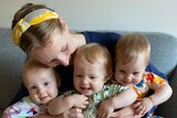 Silje Andersen-Cooke sits on a couch with her one-year-old triplets on her lap 