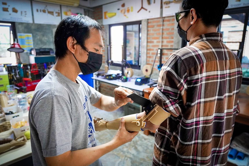 A man helps another man attach a prosthetic arm 