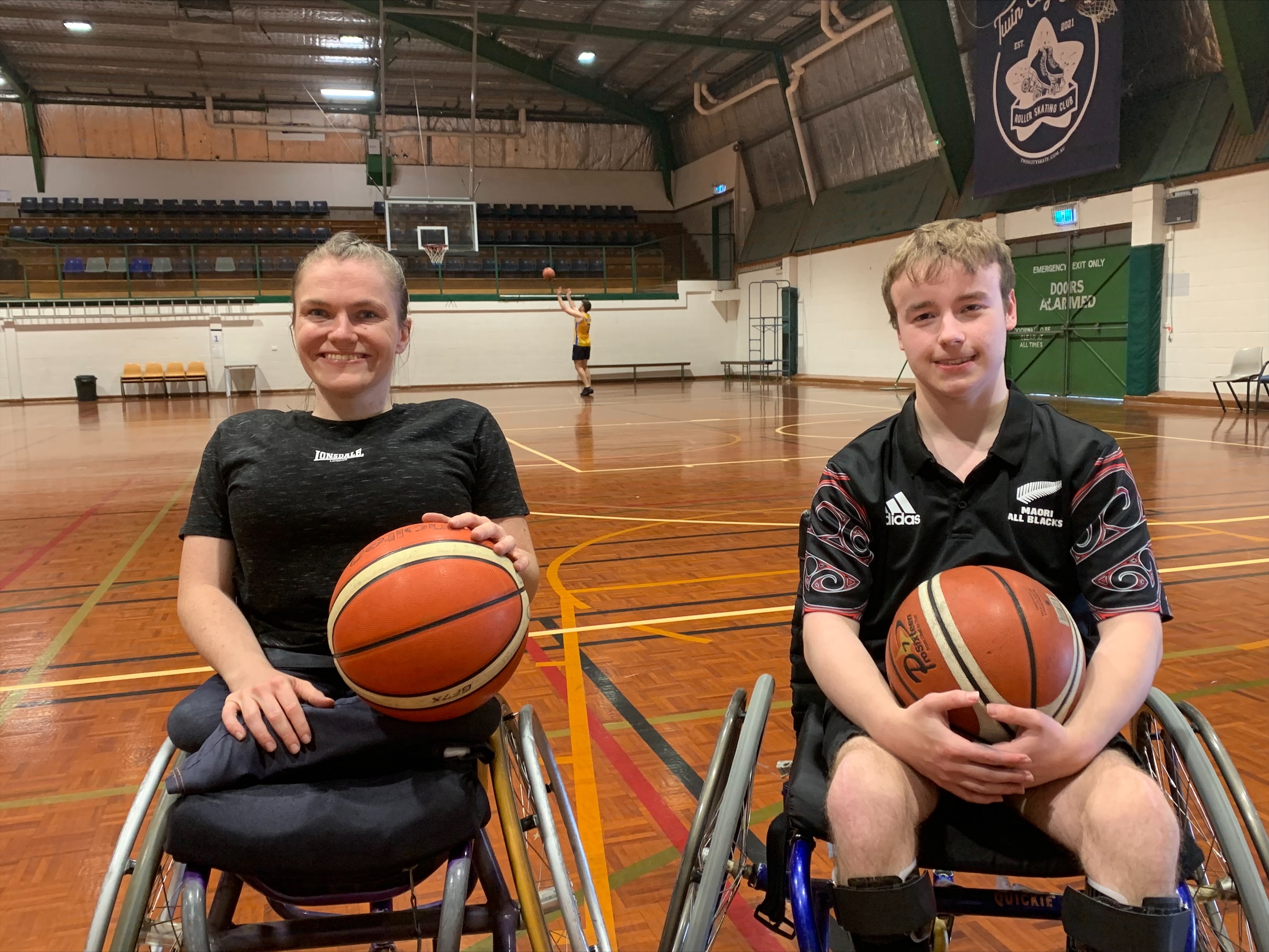 A woman and a man in their wheelchairs holding basketballs smile at the camera