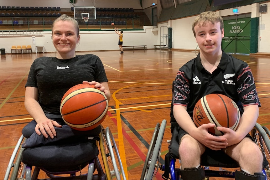 A woman and a man in their wheelchairs holding basketballs smile at the camera