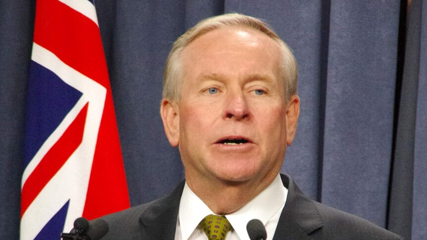 Premier Colin Barnett stands in front of a flag as he announces his Treasurer's resignation