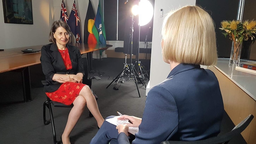 NSW Premier Gladys Berejiklian, brown hair and a red shirt, with ABC's Ashleigh Raper, a blonde woman from the back