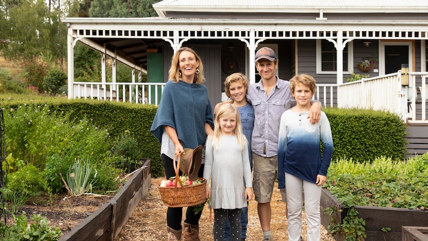 A family of a woman, a man and three children stand in front of a house. 