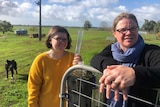 A woman wearing a blue scarf alongside a girl in a yellow jumper stand by a gate in a paddock.