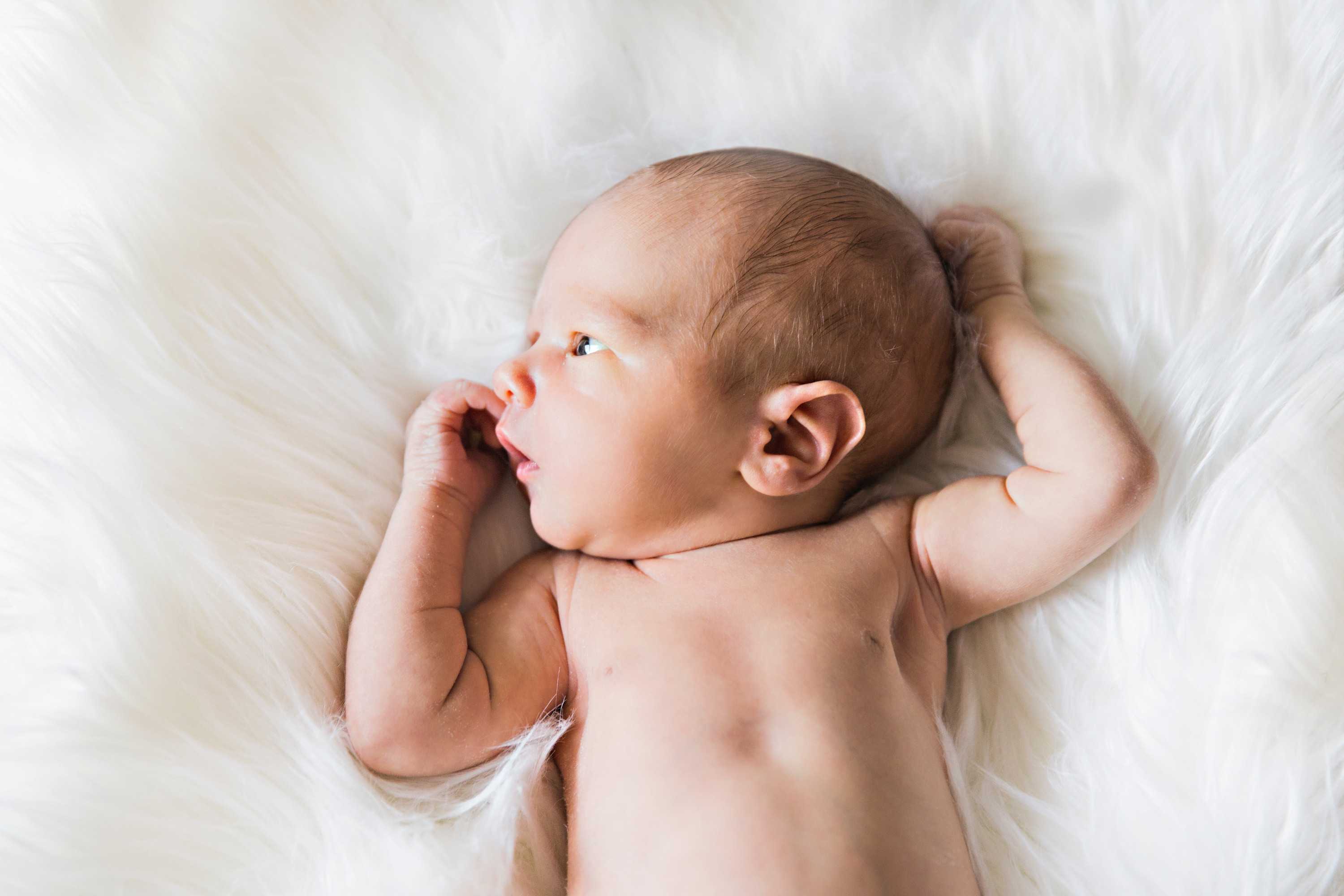 一个婴儿仰面躺在毛茸茸的白色毯子上，听听关于精子捐献的故事。 “ class=