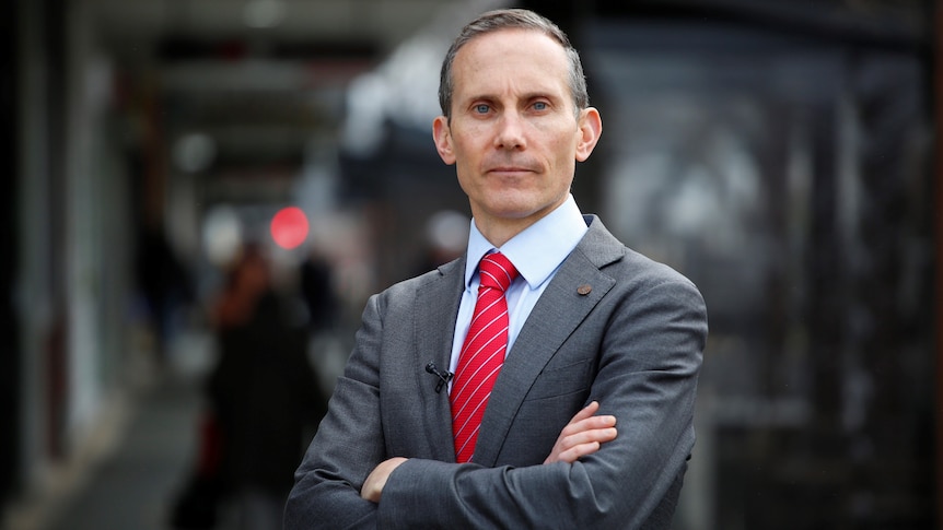 Andrew Fenner wearing a suit and red tie with his arms crossed