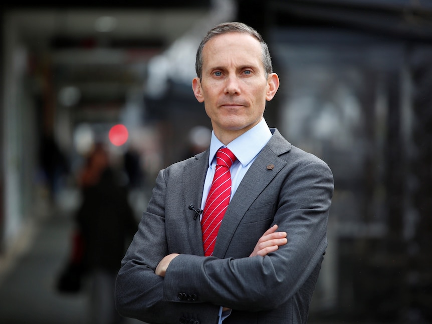 Andrew Leigh wearing a suit and red tie with his arms crossed