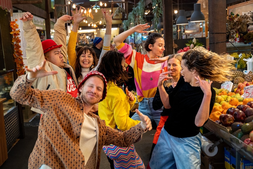 A group of young adults in colourful clothes dancing at the grocery markets.