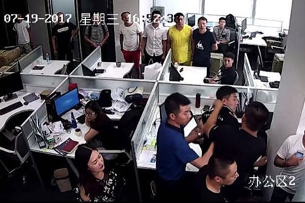 A still image from security footage shows people crowded around cubicles inside an office.
