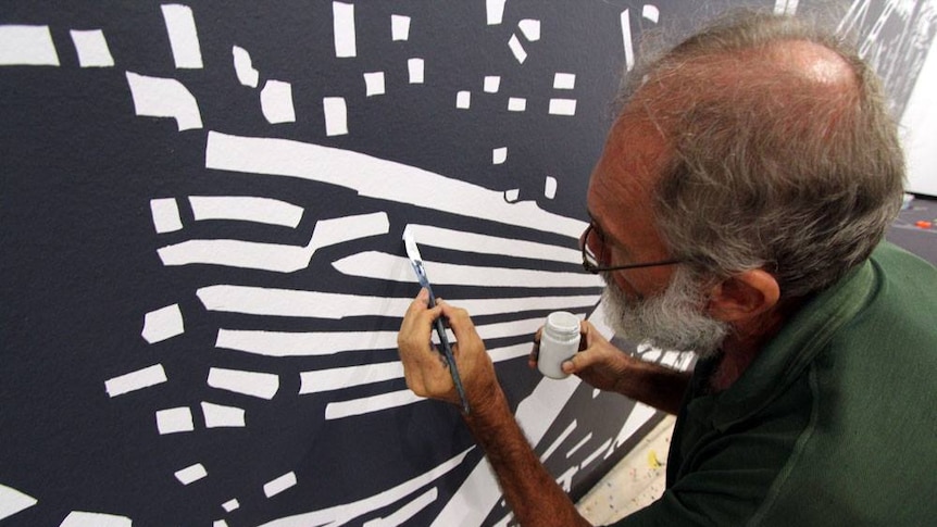 A man with a paintbrush works on a wall mural.