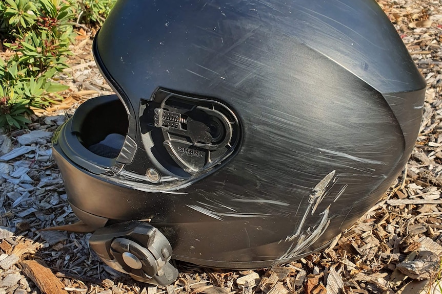 a black motorbike helmet with deep scratches in the plastic after a crash