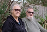 Tammy (left) and Stuart Leamer sit outside with plants and a fence in the background.