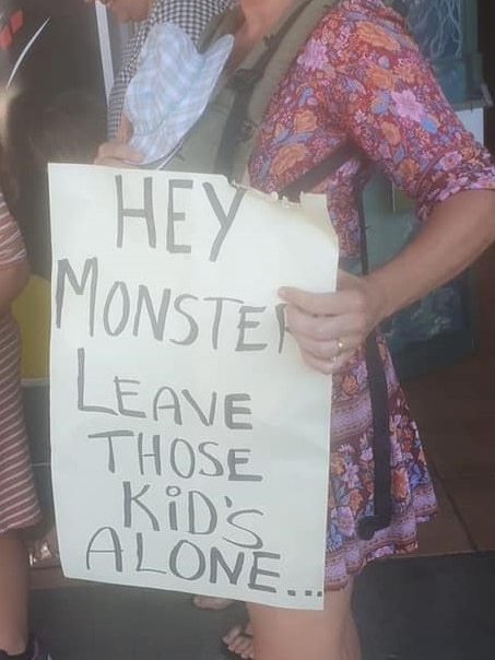 A woman holds a sign that says 'hey monsters, leave those kids alone'.