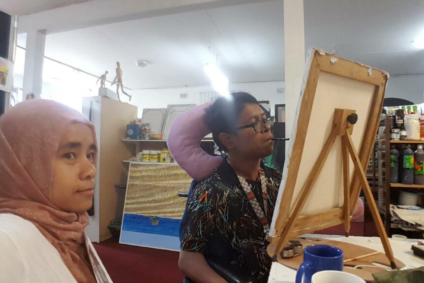 Faisal Rusdi paints with his mouth as his wife Cucu Saidah looks on.
