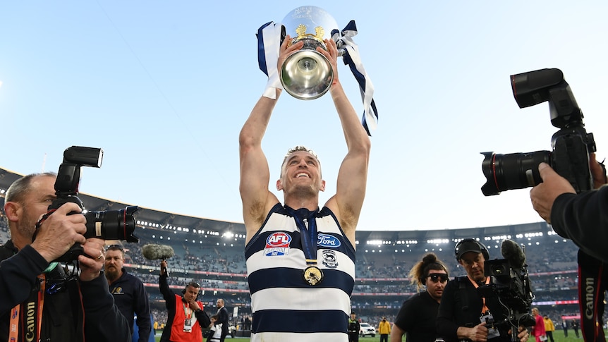 Joel Selwood smiles as he holds the premiership cup over his head and looks into the crowd