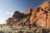 A white ochre design on the side of a red rock in an arid, desert setting.
