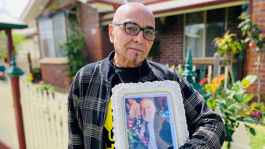 Dragan Markovic stands outside a house with a framed photograph of his father, Nenad.