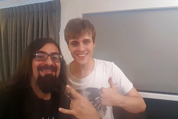 Two men give the thumbs up while taking a selfie inside a hotel room.