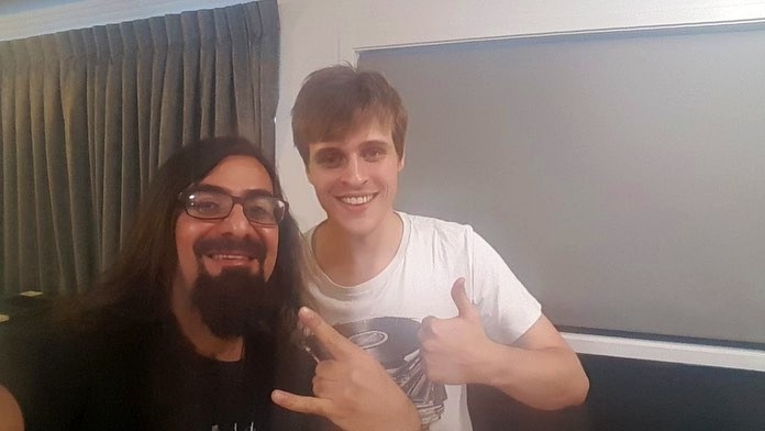 Two men give the thumbs up while taking a selfie inside a hotel room.