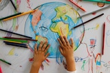 A child drawing with colour pencils a picture of Earth.