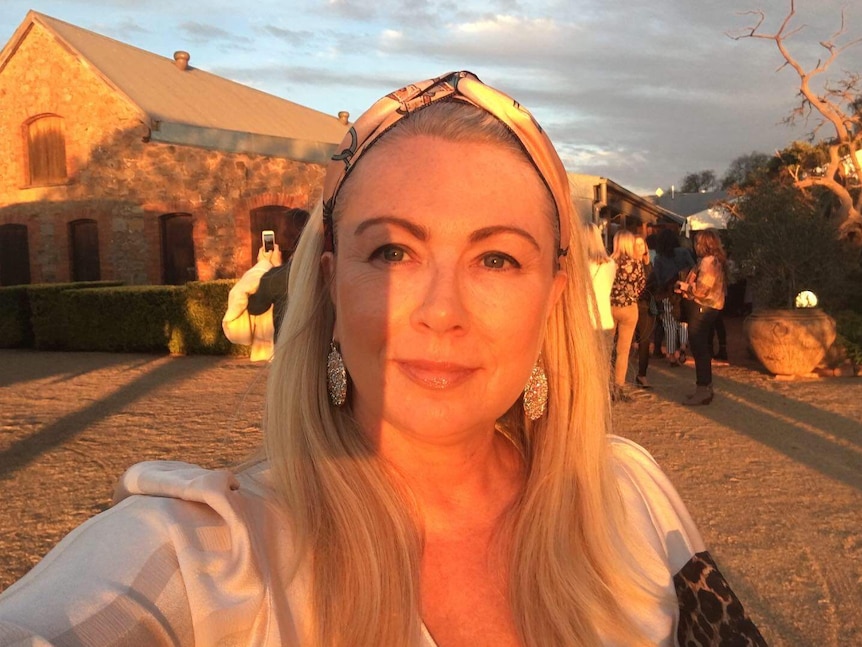 A woman with blonde hair and a head band outside in the late afternoon sun with a house in the background