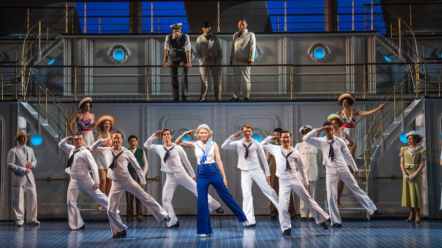 Group of sailors saluting on stage with women and men looking on and smiling in the background