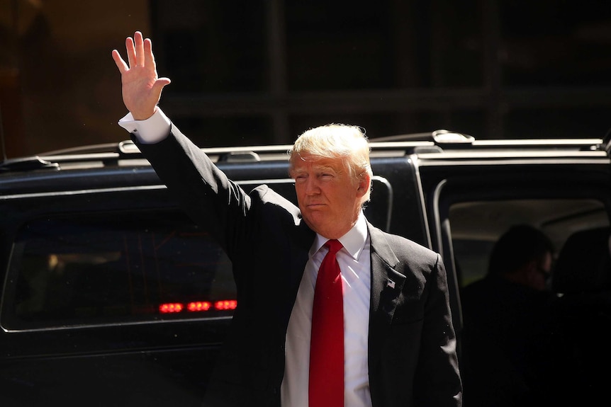 Donald Trump waves while standing next to his car.