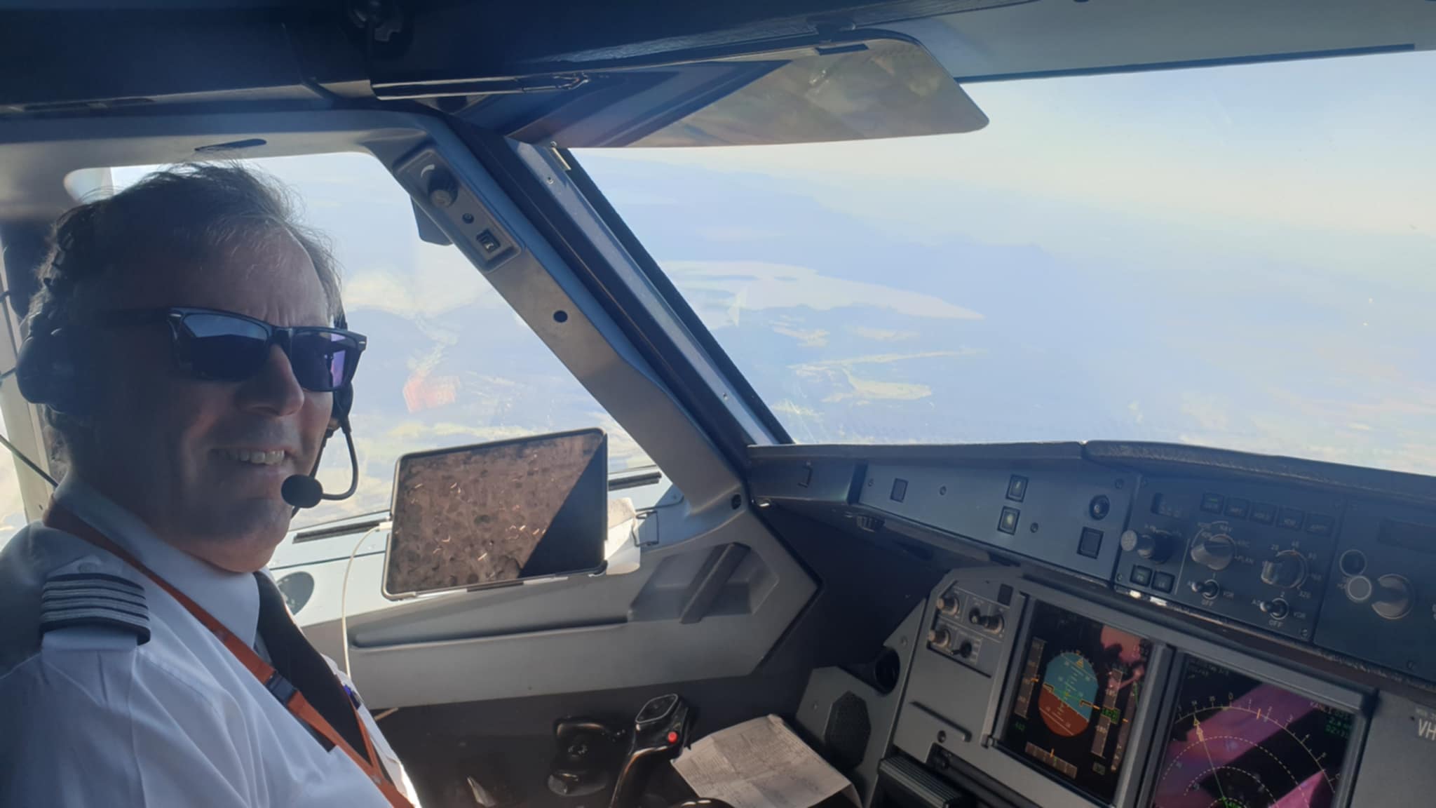 Mr Klouth sitting in the occkpit of an aeroplane wearing a headset with blue sky around.