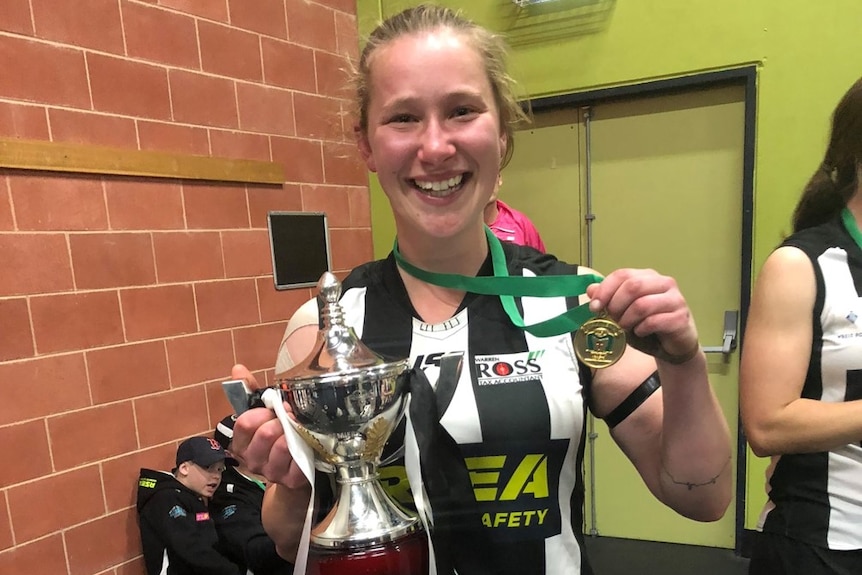 A young female footballer holds a grand final trophy