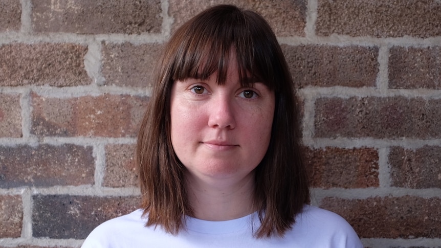 A headshot of a brunette woman with shoulder-length hair and a white tshirt.