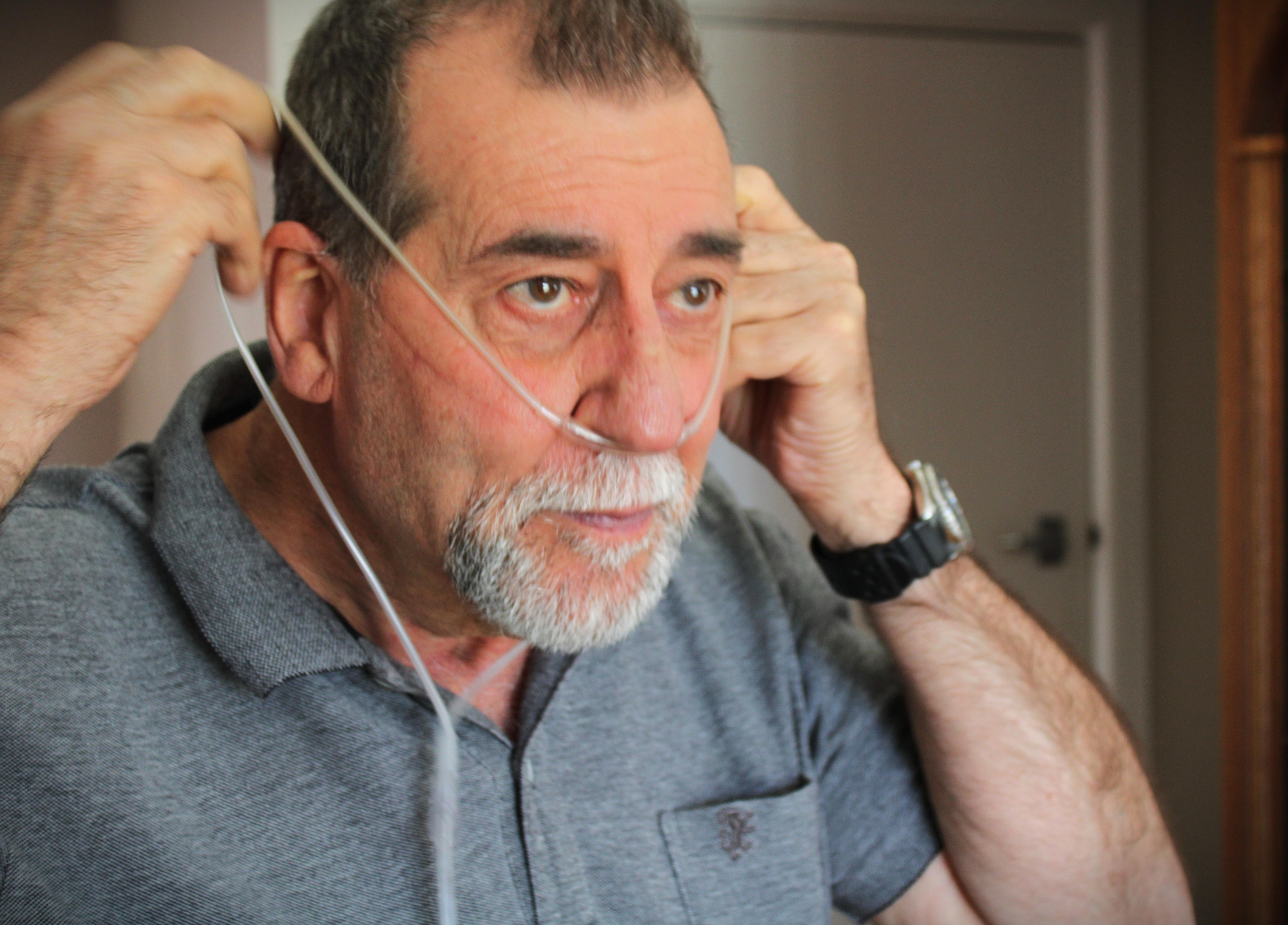 Grey haired man wearing grey shirt putting on nasotracheal tube around nose and ears