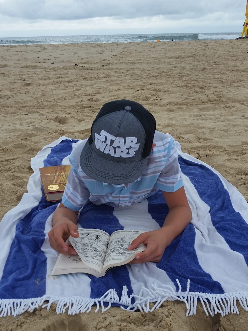 A boy reads a book on the beach in Queensland on Christmas Day.