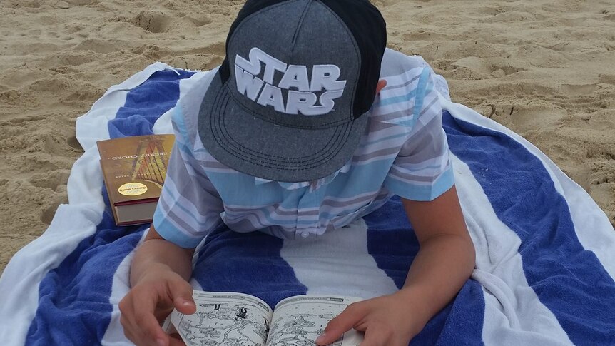 A boy reads a book on the beach in Queensland on Christmas Day.
