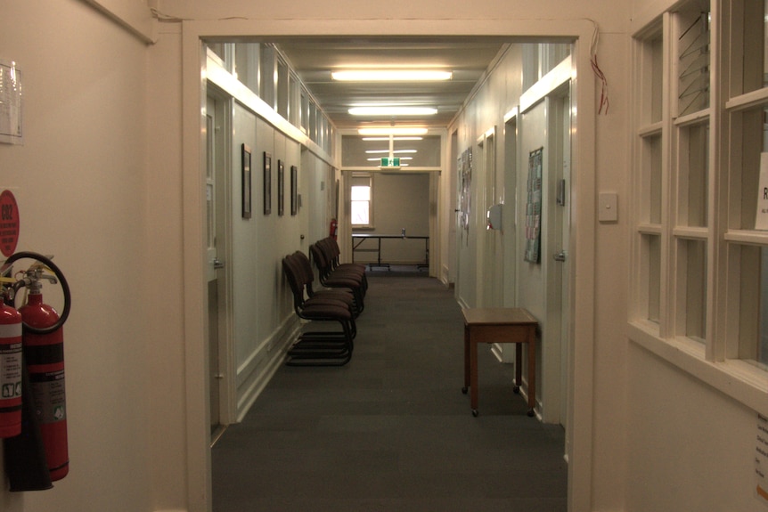 A waiting room corridor, flanked with chairs, the ceiling lined with fluorescent lights