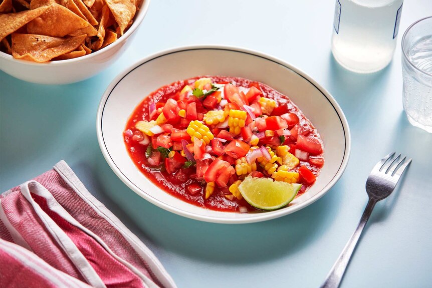 Tomato salad salsa in a bowl with a wedge of lime and corn chips