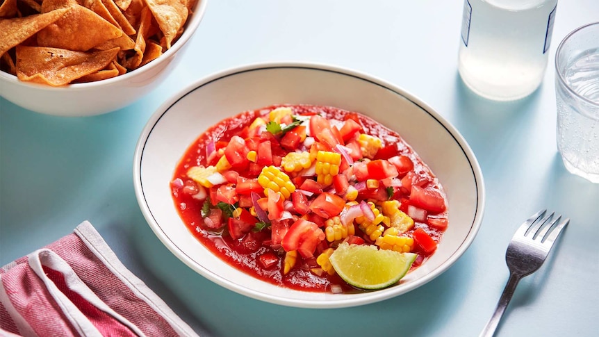 Tomato salad salsa in a bowl with a wedge of lime and corn chips