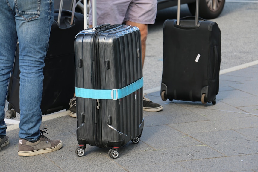 A close-up shot of suitcases and legs on a footpath.
