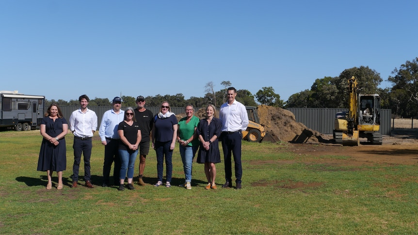 A group of people stand together in a field on a sunny day.