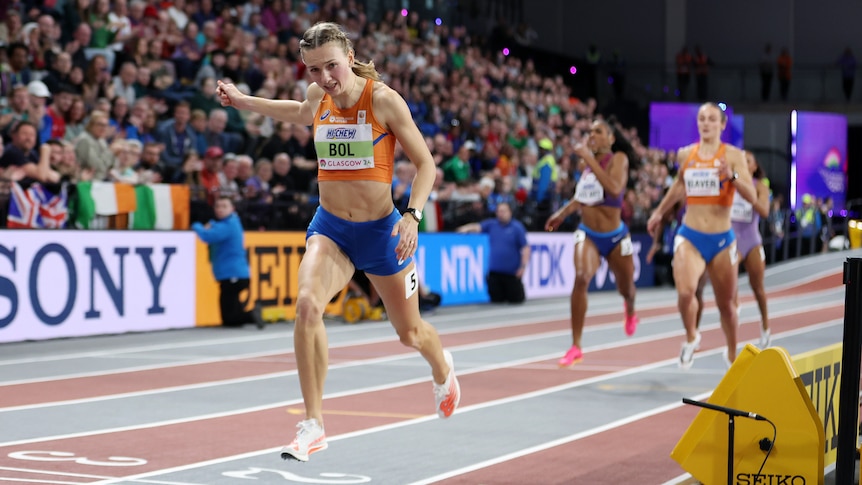 A Dutch athlete dips her head as she crosses the line to win a race on an indoor track.