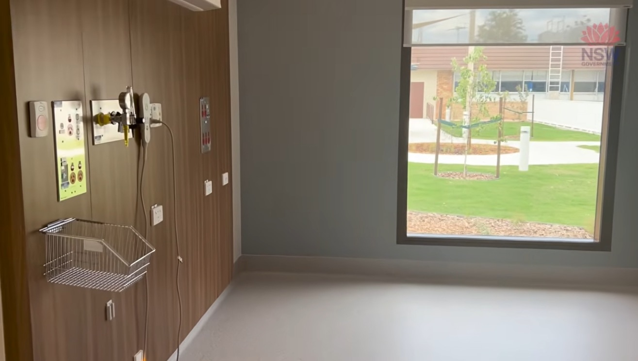 An empty, very clean and brand new maternity bedroom, with multiple plugs on the wall, and a window looking out on a nice lawn.